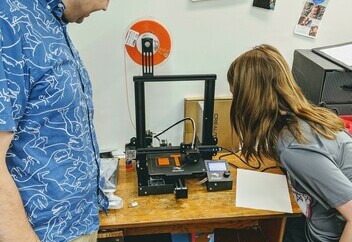 Teacher and student watch 3D printer in action