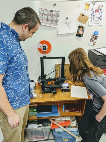 Teacher and student watch 3D printer in action